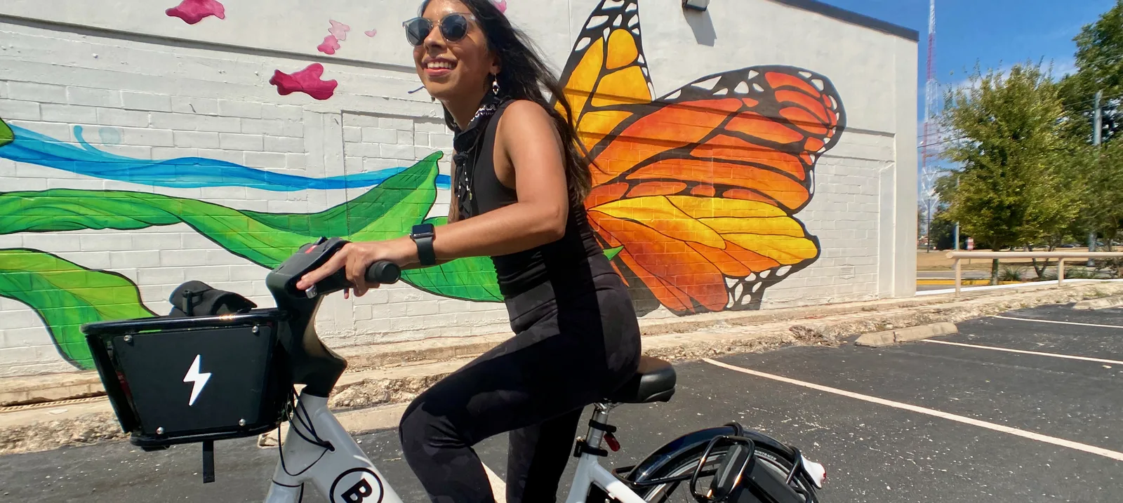 woman riding a bike share bicycle in front of a wall painted with a monarch butterfly